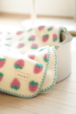A cat blanket in white with pink and green strawberry puff print